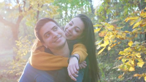 A young woman is on piggy back ride with her boyfriend in sunny autumn forest. They are flirting and smiling