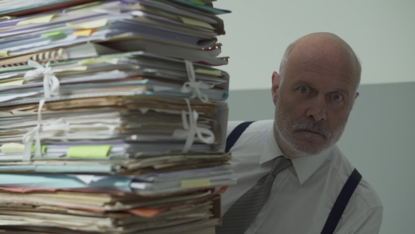 Stressed frustrated businessman sitting at office desk and peeking from behind a pile of paperwork, overwork and management concept | Shutterstock HD Video #1039113998