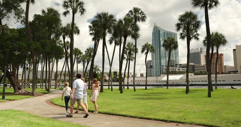 Tampa, Florida - June 14, 2019: 
 People walk along a park path near the downtown city skyline view of Tampa Florida USA looking over Plant Park and the Convention Center Riverwalk