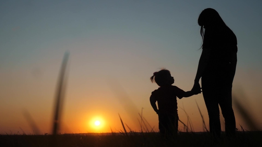 happy family funny a mom holds daughter hands silhouette at sunset slow motion. little girl and woman mom look at each other outdoors sunlight on the field outdoors. teamwork happy family mom takes