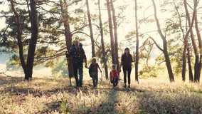 happy family walking through the forest navigation tourists with wooden sticks with backpacks teamwork and children slow motion video concept. father mom dad son and daughter come with wooden