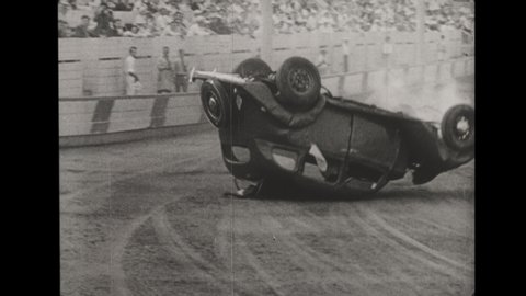 1920s Ford Tudor Crashes Head-On into another Ford Tudor. A Stuntman Drives Car into Stadium, Jumps Ramp, Crashes and Flips Car as Crowd of Spectators Cheers On. 
