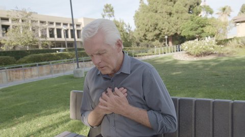 Closeup portrait of senior man having excruciating crushing chest pain on bench, isolated outdoors outside background at park