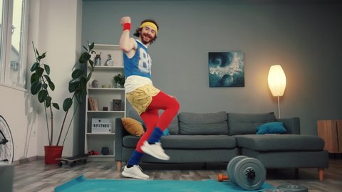 LOS ANGELES, CALIFORNIA, 10 OCTOBER, 2019: Crazy emotional funny athlete warming up and dancing to cool music on exercise mat in the living room.