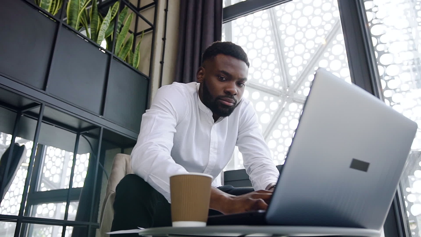 Purposeful handsome bearded african american businessman typing on the laptop in specially designated office room with soothing design