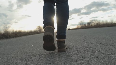 Girl is walking down an empty road in the sun, feet, boots, steadicam shot
