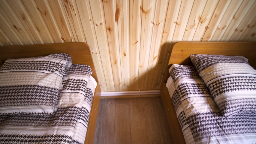 The interior of a small clean hotel room with two beds, cheap lodging concept. Art. A room with wooden walls and floor and two narrow beds.