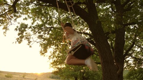 child swinging on a swing in park in sun. teen girl enjoys flight on swing on summer evening in forest. concept of happy childhood.