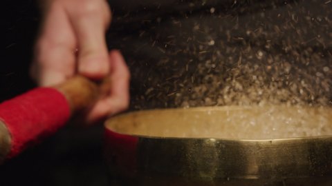 A healer strikes a singing bowl with some water causing it to vibrate producing healing sounds and frequencies. Spirituality, therapy and alternative medicine concepts. Filmed on Red Camera, Slow mo.