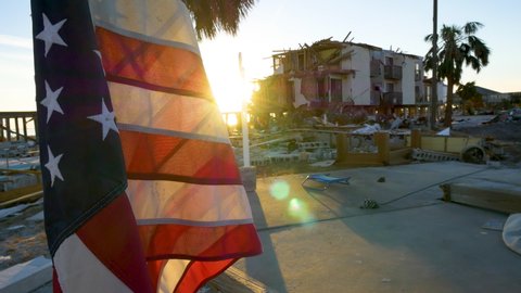 Mexico Beach , Florida / United States - 10 17 2018: Bright morning sun flair shines behind American flag surrounded by rubble and a ruined house in the aftermath of Hurricane Michael in Mexico Beach,