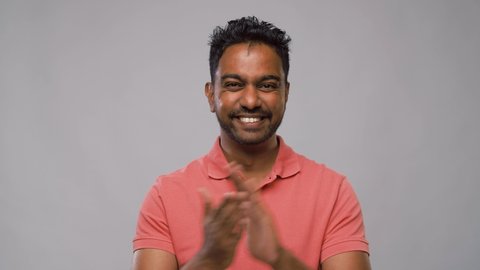 success, emotion and appreciation concept - happy young indian man applauding and showing thumbs up over grey background