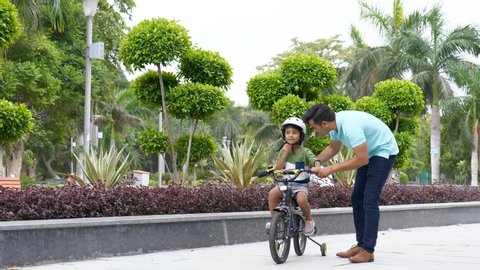 Young Indian father teaching his son how to ride a bicycle on a footpath 