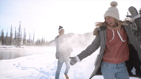 Slow motion: Playful young couple throwing snowballs at each other at sunset having fun and enjoying winter vacations