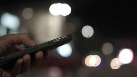 Smartphone on a blur background.  Woman's hand dials the phone number against the lights of the night city.