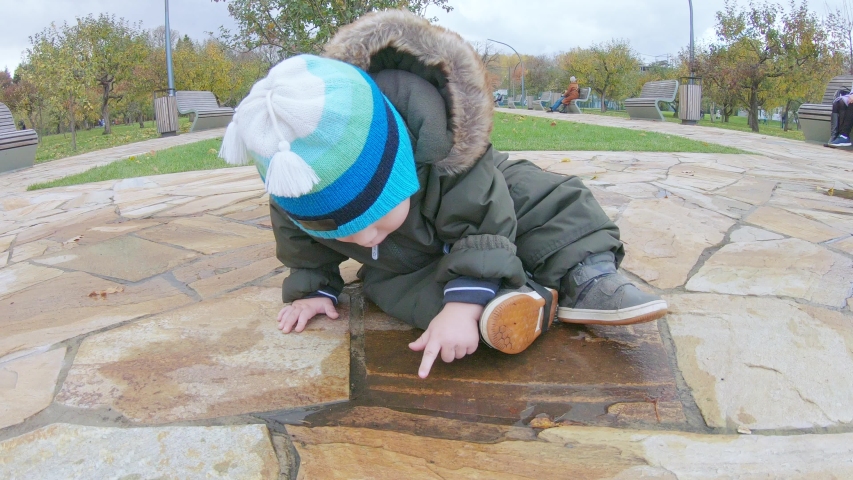 Infant boy sits on marble tiles in the park and touches the water in a puddle