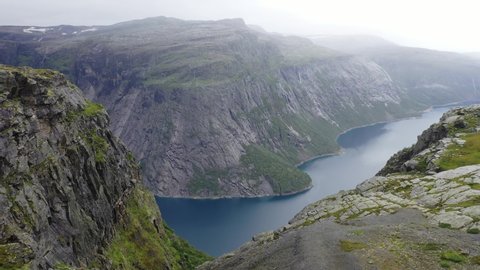 Norway. Trolltunga. Ringedalsfossen. Video from the drone. The drone flies along the mountain and overlooks the fjord. Bright green grass, summer. Waterfalls flow down from the mountains. Thick fog.  