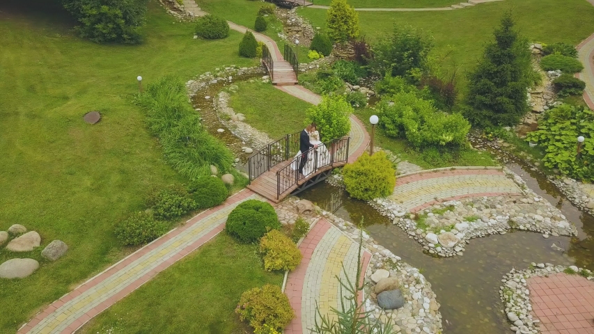 happy just married couple on little bridge over stream in green park on warm sunny day aerial view