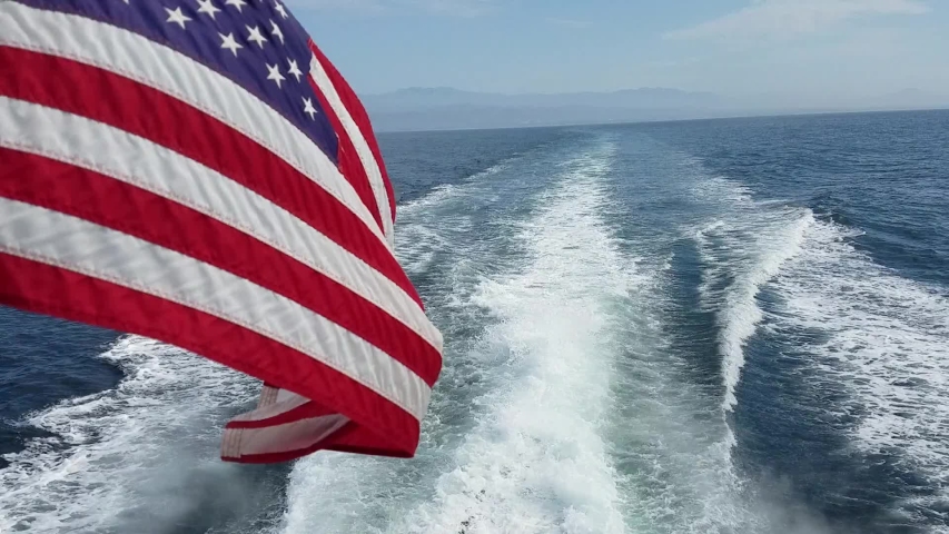 American flag waving and the water wake done by a speeding boat slicing the Pacific ocean near Ventura, California, on a ride to the Channel Islands National Park

