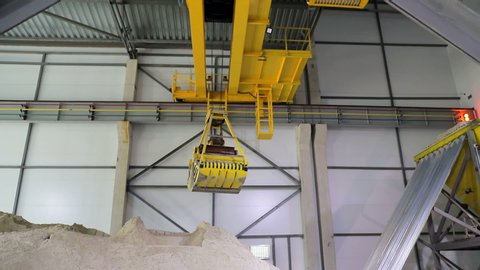 A huge radio-controlled bucket, grabs the sand and pours it into a large sand storage hangar.