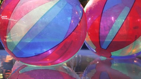 Big plastic bubbles on water for children. Zorbing in swimming pool. Colorful multi-colored, blue and red balloons. Night light. Favourite children's water activities. Night reflection in the water.