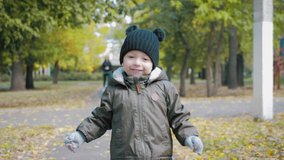 Happy baby boy running in autumnal park. Little child playing on autumn walk. Autumnal forest with golden leaves. Steadicam video, 4K slow motion.