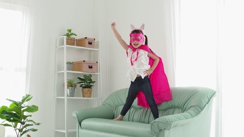 Little asian girl in superhero costume with mask playing in living room 