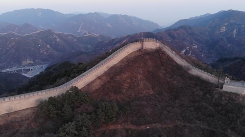 Aerial view of Badaling Great Wall of China at sunset hour, watch tower on top of hill. Thin line of the wall seen running over mountains on background. Famous Chinese landmark at early spring season