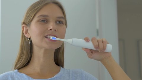 A static footage showing a young pretty woman brushing her teeth with an electronic toothbrush. Concept of dental care and hygiene.