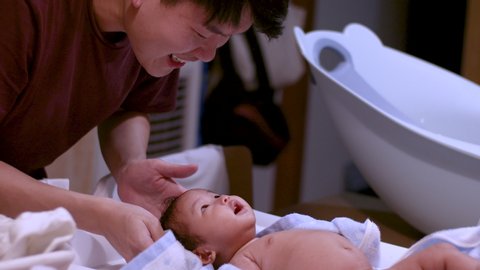 Asian parents drying their infant baby girl after a bath at home, warm and happy, cozy, towel, baby lying down on a table , fluorescent light, day time