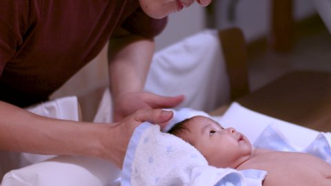 Asian father drying his infant baby girl's hair after a bath at home, warm and happy, cozy, towel, baby lying down on a table , fluorescent light, day time