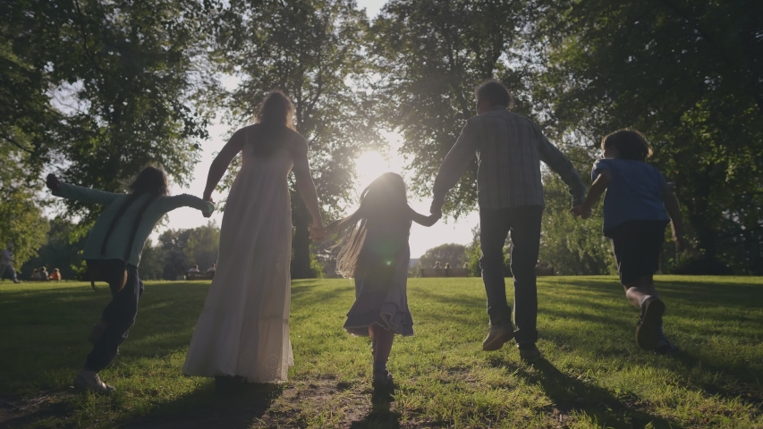 Silhouetted happy caucasian family running towards sun having fun in city park at sunset. Slow Motion. Family, Motherhood, childhood, freedom, future and travel concept. Brother, sisters and parents Royalty-Free Stock Footage #1039232021