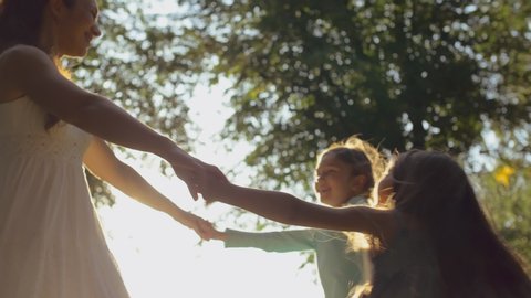 Mother and two daughters dance in a circle holding hands in summer park