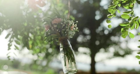 bouquet of flowers in a glass bottle hangs on a tree. Wedding decor at an exit ceremony
