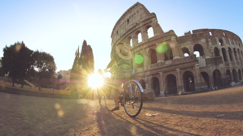 Three happy young women friends tourists riding bikes at Colosseum in Rome, Italy at sunrise.