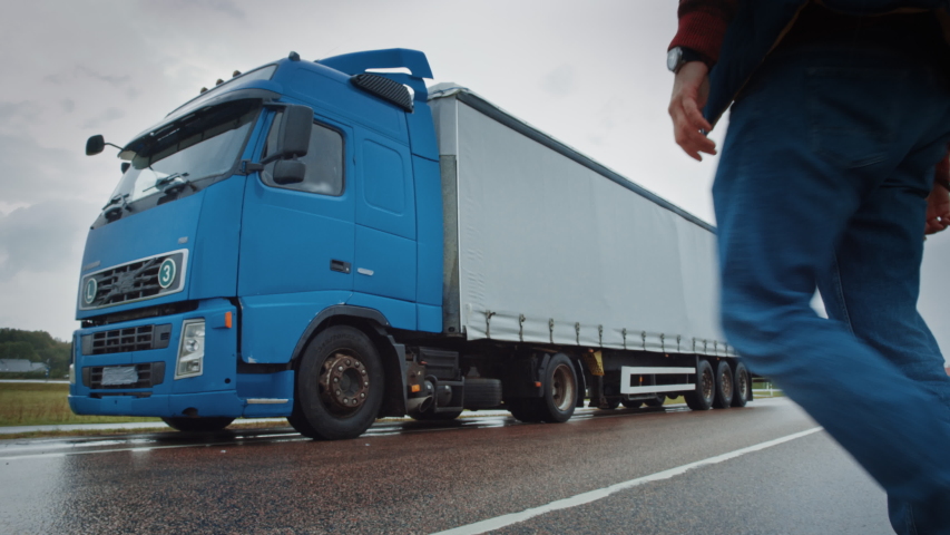 Truck Driver Crosses the Road in the Rural Area and Gets into His Blue Long Haul Semi-Truck with Cargo Trailer Attached. Logistics Company Moving Goods Across Countrie and Continent Royalty-Free Stock Footage #1039239764