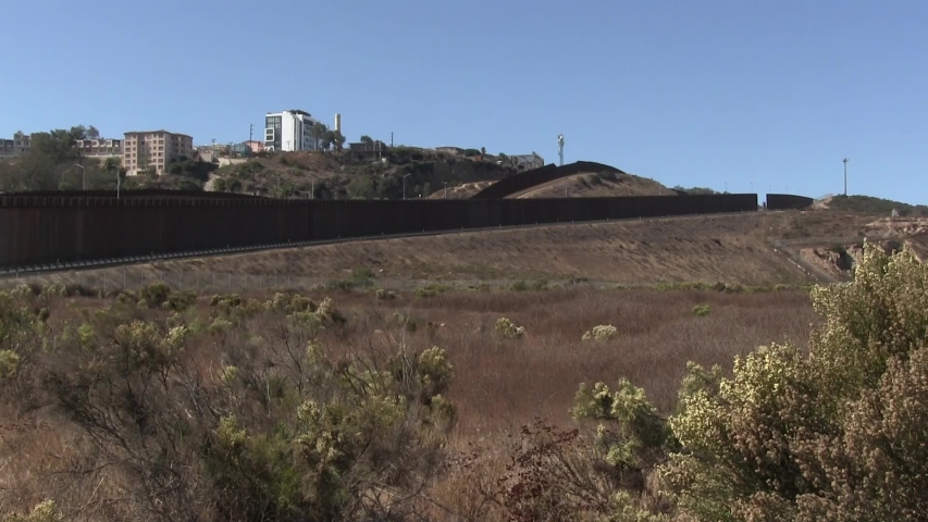 Multiple U.S. Mexico border walls between San Diego and Tijuana looking southwest with shrubbery and buildings in Mexico.