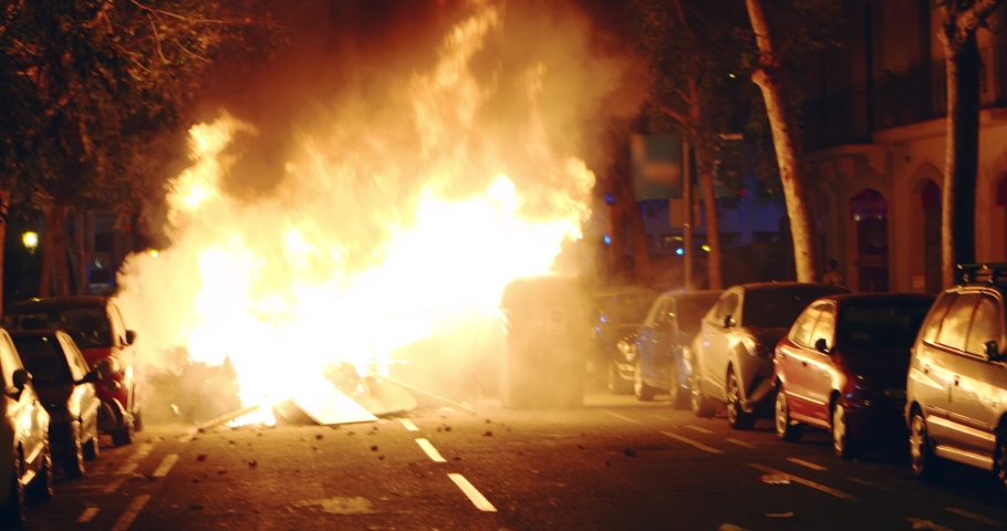 Young rebel riot revolutionary anarchist stands on trash and fire showing fuck as protest for independence on demonstration about the proces and political prisoners Demonstrator burns garbage bins War