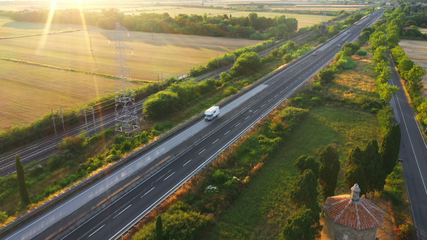 Aerial Drone Footage: Long Haul Semi Trucks Driving on the Busy Highway in the Rural Region of Italy. Agricultural Crop Fields and Hills in the Background Royalty-Free Stock Footage #1039245149