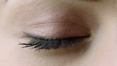 Women's young eye with black mascara on long lashes. Nude eyeshadow and black liner makes a make up. Closed right eye macro, prores444, 24fps, RAW, Arri Alexa mini
