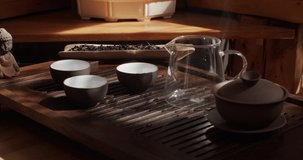 4k still-life video shot of Chinese tea ceremony preparation slow motion of steaming smoke. Black and white crockery set close up with pot cups standing on bamboo table equipment. Caffeine energy 

