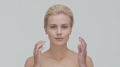 Studio portrait of young, beautiful and natural blond woman applying skin care cream. Face lifting, cosmetics and make-up.