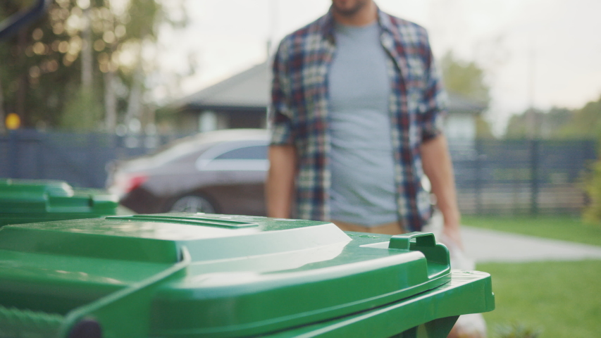 Close Up Shot of a Caucasian Male in Checkered Shirt Throwing Away Biological Food Waste into a Green Trash Bin. He Uses Correct Garbage Bin Because He is Sorting Waste and Helping the Environment. Royalty-Free Stock Footage #1039252379