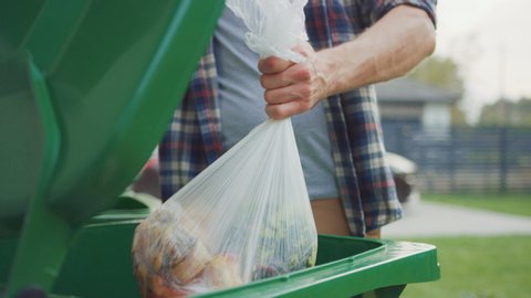 Close Up Shot of a Caucasian Male in Checkered Shirt Throwing Away Biological Food Waste into a Green Trash Bin. He Uses Correct Garbage Bin Because He is Sorting Waste and Helping the Environment.