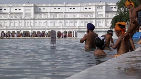Punjab / India - 10 02 2019: Children And Adults Taking Purifying Bath in lake surrounding the Golden Temple of Amritsar, India. Low Angle