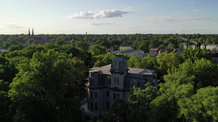 Aerial dolly zoom in on residential white mansion building and lush background