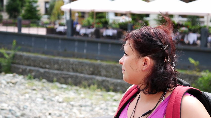 A woman stands on a bridge and looks at a mountain river.