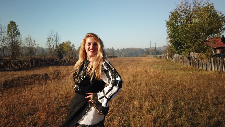 Beautiful happy blonde hair girl dancing dressed with the traditional Romanian dress looking at camera. AUTUMN Romania travel footage.