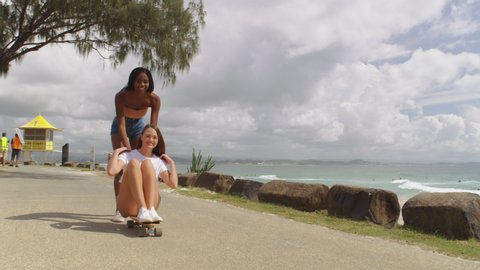 Young girls millennials fooling around on skateboard at the beach with ocean in the background. Medium close on 4k RED camera.