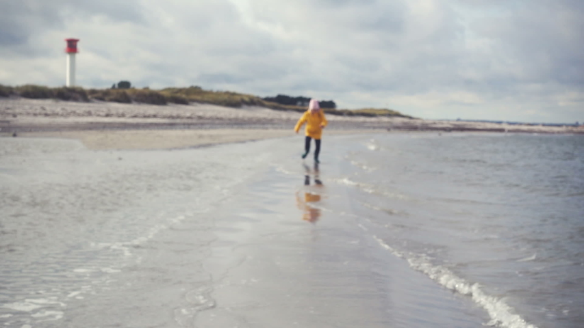 Joyful brother and sister running in water of Baltic sea in northern Germany. Lighthouse on background Royalty-Free Stock Footage #1039294673
