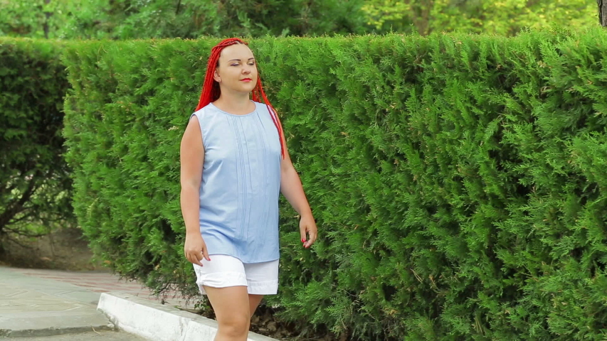 A woman with red hair walks along the green spaces